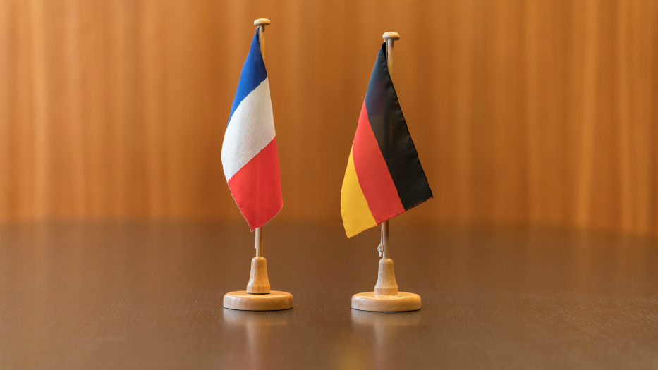 Auf einem Tisch stehen zwei kleine Tischflaggen mit den Flaggen Frankreichs und Deutschlands nebeneinander